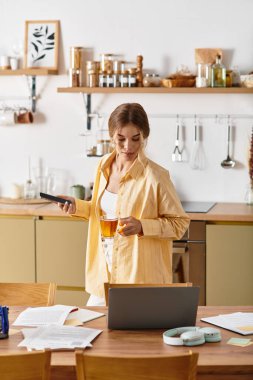 Sıcak bir mutfakta genç bir kadın gündüzleri içki ve dijital cihazla birden fazla iş yapıyor..