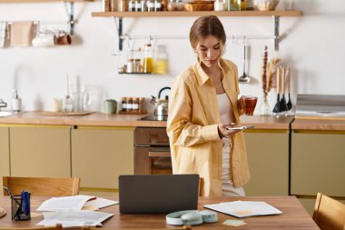 Samimi bir mutfakta, güzel bir kadın telefonuna bakarken çay yudumlarken biraz dinlenir..