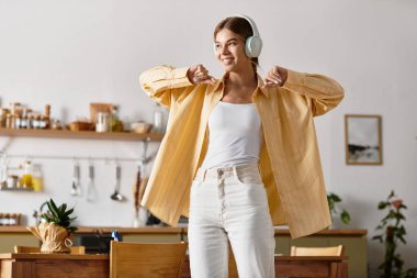 Neşeli ve neşeli genç bir kadın mutfağında neşeyle dans ediyor, en sevdiği melodilerin tadını çıkarıyor..