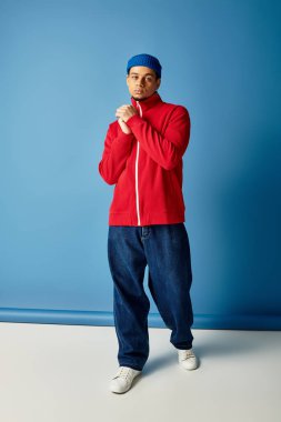 Genç bir adam, mavi arka planda beresi olan modaya uygun bir şekilde poz veriyor..