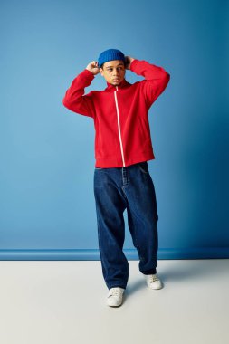 Tarz sahibi genç bir siyah adam bereyle parlak mavi bir arka plana karşı güvenle poz verir..