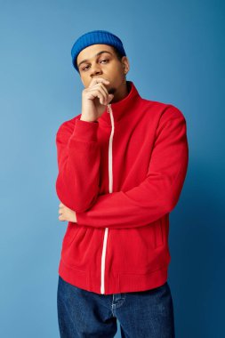 Şık bir genç adam düşünceli, çarpıcı mavi bir ortamda şehir modasını sergiliyor..