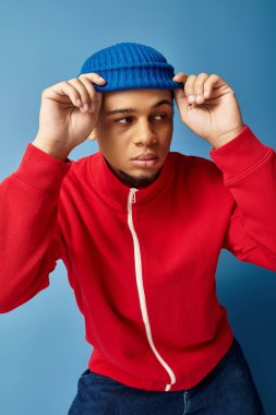 Havalı bir Afrikalı genç Amerikalı, modaya uygun kıyafetini sergilerken mavi beresini ayarlıyor..