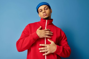 Moda düşkünü Afro-Amerikan bir adam stilini gösteriyor. Mavi bir bere ve kırmızı bir ceket giyiyor..