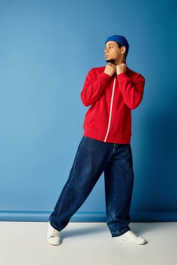 Kendine güveni tam, şık giyinmiş genç bir adam cesur mavi bir arkaplanda duruyor..