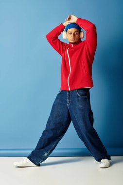 Şık bir genç adam kırmızı ceketli ve bereli, kendine güvenen bir poz veriyor. Tarzını vurguluyor..