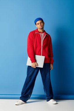 Tarz sahibi genç siyah bir adam, kendine güvenen bir şekilde dizüstü bilgisayarla poz veriyor..