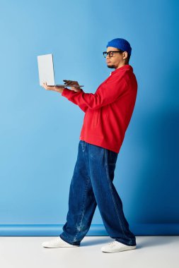 Kırmızı kazaklı ve mavi bereli şık bir genç adam laptopuyla yaratıcı bir şekilde meşgul oluyor..