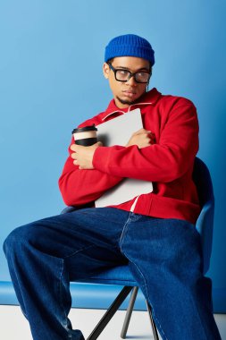 Mavi bereli şık bir genç adam elinde bir defter ve kahve fincanı tutarak düşünceli bir şekilde oturur..