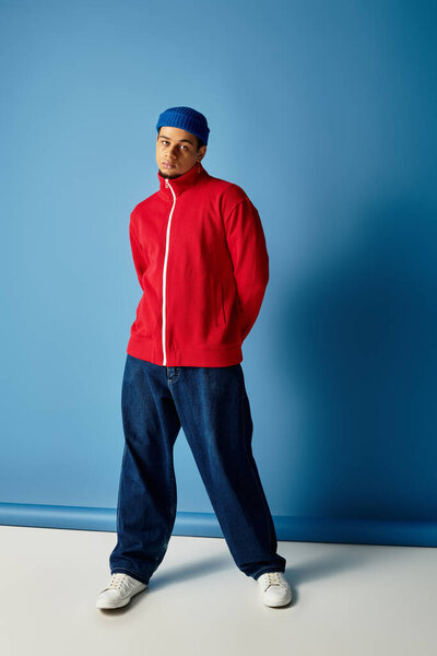 Модный молодой человек демонстрирует свой уникальный стиль в яркой красной куртке и синей шапочке.