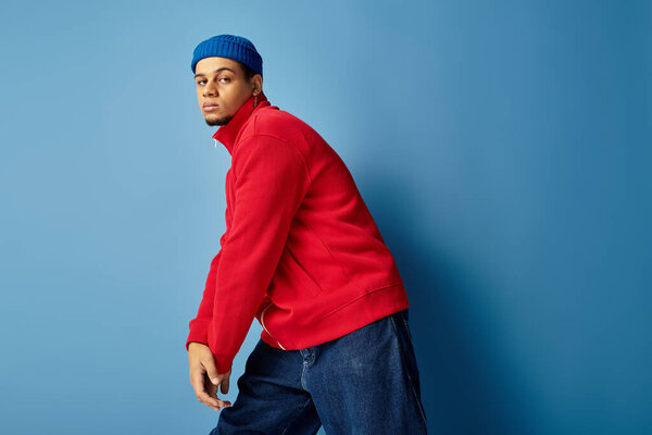 A stylish young man with a beanie poses confidently against a smooth blue background.