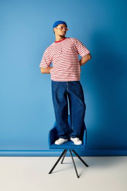 Genç Afro-Amerikalı bir adam kendine güvenerek sandalyede poz veriyor, modaya uygun tarzını sergiliyor..