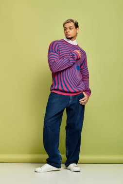 Genç siyahi bir adam yeşil bir arkaplana karşı renkli çizgili bir kazakla güvenle poz veriyor..