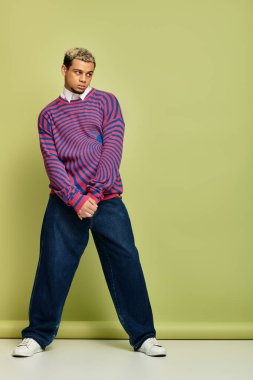 Tarz sahibi genç adam, modaya uygun, soyut çizgili kazak ve rahat kot pantolon giyer..