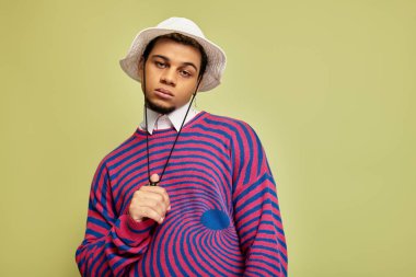 Genç siyahi bir adam, yeşil bir arka planda şık, soyut çizgili bir kazak mankenliği yapıyor..