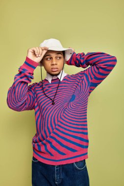 Tarz sahibi genç siyahi bir adam yeşil bir zemine karşı kendine güvenen çizgili bir kazakla poz verir..