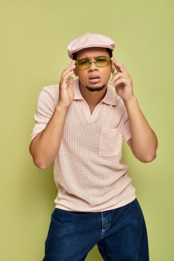Tarz sahibi genç siyahi bir adam pembe polo gömleği ve düz şapkasıyla görünüşünü sergiliyor..