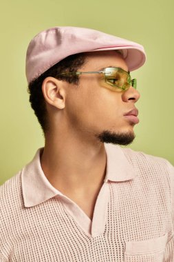 Kendinden emin Afro-Amerikalı bir adam pembe polo gömlek ve düz şapka giyiyor..