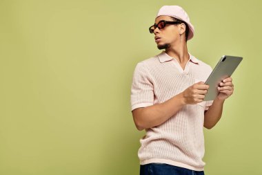 Pembe polo gömlekli ve düz şapkalı şık bir genç adam bir tablet taşıyor, kendine güveni ve yeteneği var..