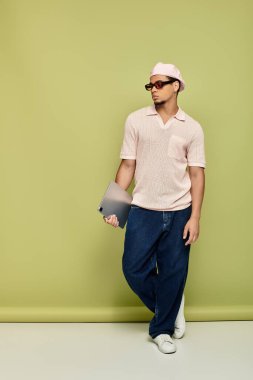 Tarz sahibi genç siyahi bir adam canlı yeşil bir zemine karşı kendinden emin bir tablet tutuyor..