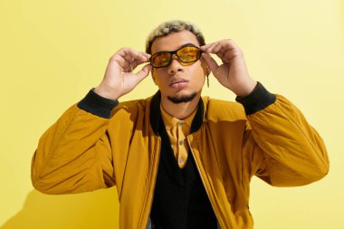 Canlı bir stüdyoda, genç bir Afrikalı Amerikalı gözlüğünü ve bombacı ceketini sergiliyor.