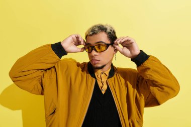 Genç bir Afrikalı Amerikalı, bir stüdyoda modaya uygun bir bombacı ceketi ve şık bir güneş gözlüğü modelliyor..