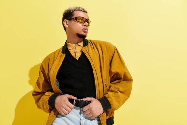 Kendine güvenen genç bir zenci şık bir bombacı ceketiyle parlak sarı bir arka plana poz veriyor..