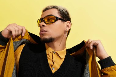 Canlı bir stüdyo ortamında, genç bir adam son moda bombacı ceketini ve güneş gözlüğünü sergiliyor..