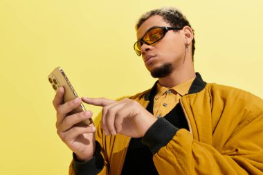 Sarı tonlarla dolu canlı bir stüdyoda, bombacı ceketli genç bir adam akıllı telefonunu kontrol ediyor..