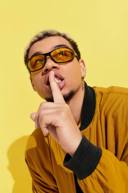 Havalı bombardıman ceketli genç adam canlı sarı bir zemin karşısında artistik bir poz veriyor..