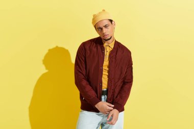 Afro-Amerikalı şık bir adam, bombardıman ceketini parlak sarı bir arka plana karşı modelliyor..