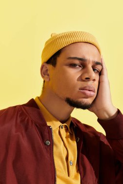 Afrikalı genç bir Amerikalı şık bir bombacı ceketi ve sarı bir bereyle rahatça poz veriyor..