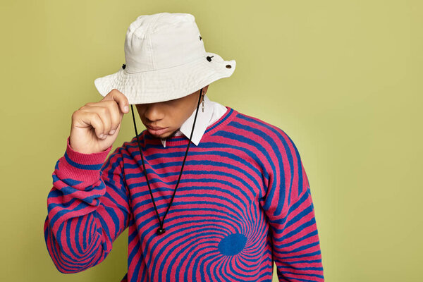 A stylish young Black man poses in an abstract striped sweatshirt against a bright green background.