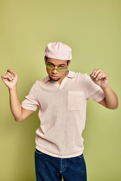 Модный молодой африканский американец уверенно позирует в розовой рубашке для поло и плоской кепке.