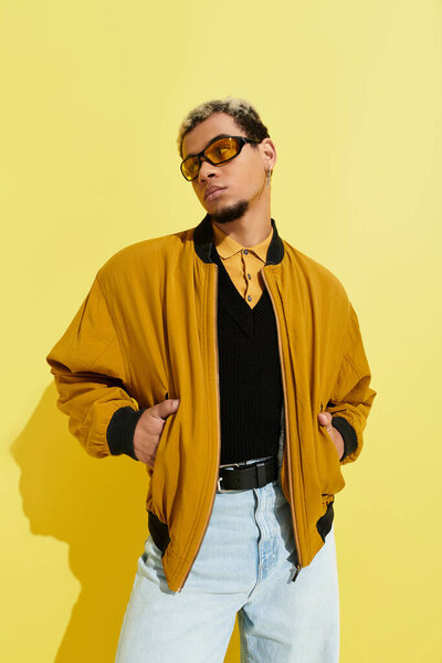 A young Black man poses confidently in a trendy bomber jacket against a yellow backdrop.
