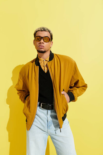 A young Black man poses confidently in a vibrant studio, wearing a stylish bomber jacket.