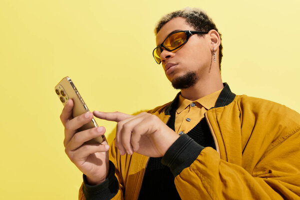 In a vibrant studio filled with yellow tones, a young man in a bomber jacket checks his smartphone.