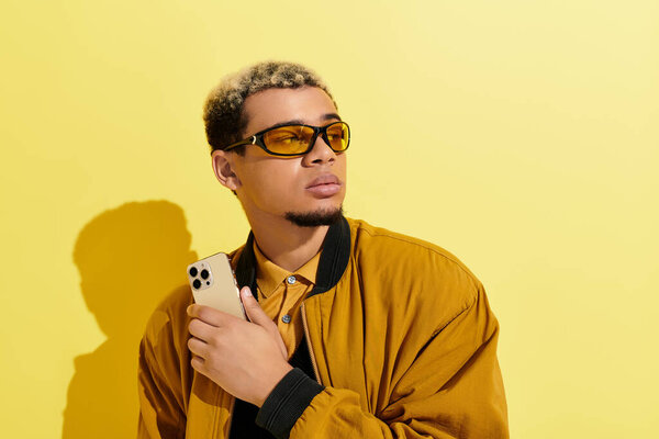 A young african american man poses confidently in a stylish bomber jacket against a yellow backdrop.