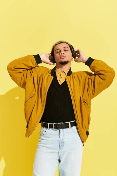 A young African American man showcases his trendy bomber jacket against a bright yellow backdrop.