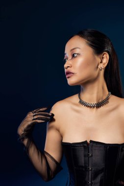 Siyah korseli ve yaratıcı makyajlı genç bir kadın mavi arka planda poz veriyor..