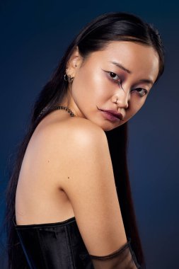 Siyah korseli genç bir kadının yaratıcı portresi mavi bir arka planda ürkütücü bir makyaj sergiliyor..