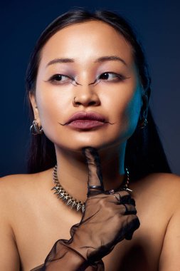 Genç bir kadın çarpıcı bir makyaj sergiliyor mavi, ürkütücü bir arkaplana karşı..