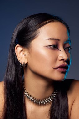 Asyalı kadın esrarengiz mavi arka planda sanatsal makyaj sergiliyor.
