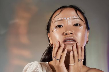 Genç bir kadın, bir stüdyo ortamında inci süslemeli makyaj yapıyor..