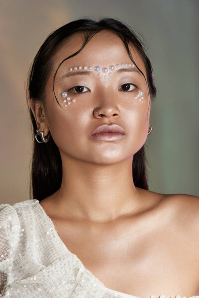 Young Asian woman showcases stunning creative makeup with pearls adorning her face in a studio.