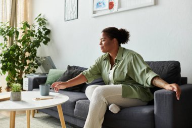 Afro-Amerikalı bir kadın evinde vakit geçirmekten zevk alıyor, çayını yudumluyor ve rahatlıyor..