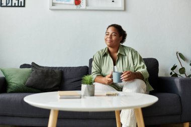 Afro-Amerikalı bir kadın şık dairesinde sakin bir öğleden sonra geçirir, kahvesini yudumlar..