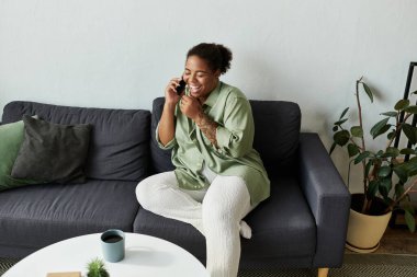 Şık dairesinde rahatça uzanırken neşeli bir kadın telefonda sohbet ediyor..