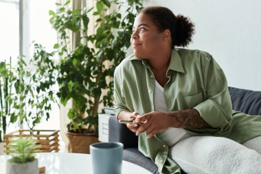 Genç bir kadın telefonunu kullanırken gülümsüyor, evdeki kanepede rahatça dinleniyor..