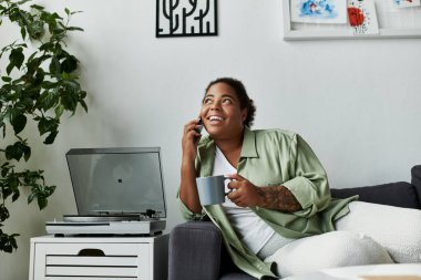 Neşeli bir kadın şık dairesinde rahatlar, kahvesini yudumlar ve telefonda sohbet eder..